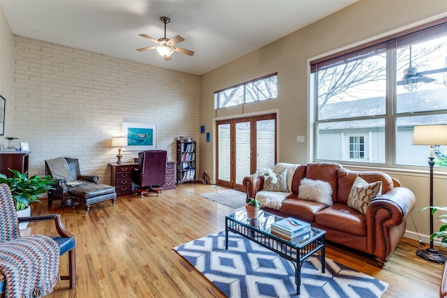 living room with brick wall, french doors, ceiling fan, and light wood-type flooring