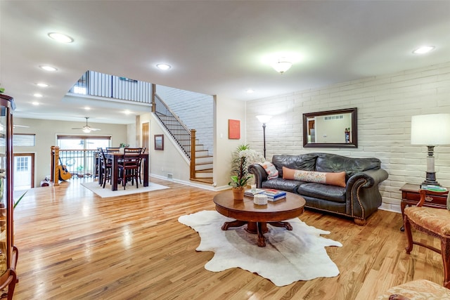 living room featuring ceiling fan, brick wall, and light wood-type flooring