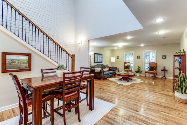 dining space with a towering ceiling, brick wall, and light hardwood / wood-style flooring