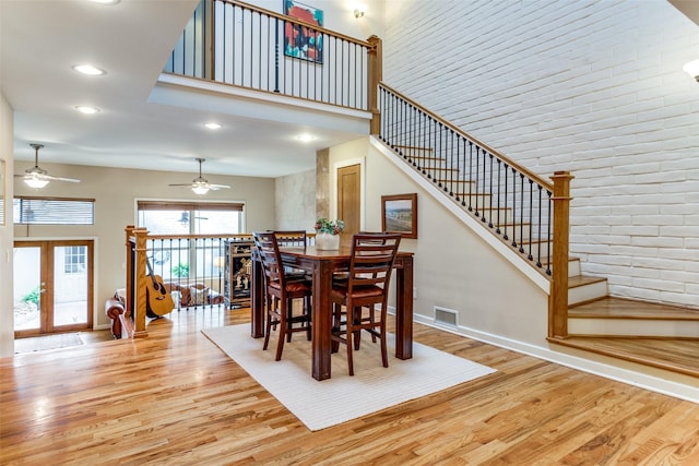 dining area with french doors, brick wall, light hardwood / wood-style floors, and a high ceiling