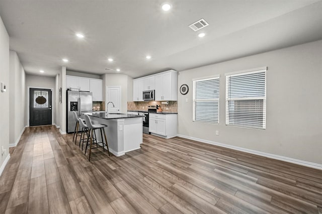 kitchen featuring appliances with stainless steel finishes, white cabinetry, sink, a kitchen breakfast bar, and a center island with sink