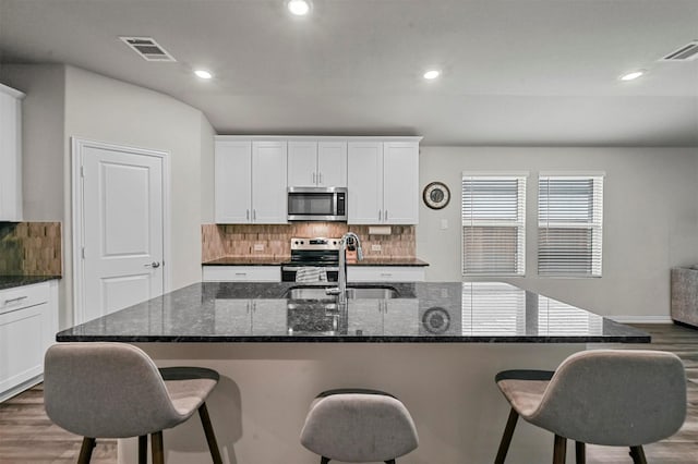 kitchen with an island with sink, white cabinetry, sink, dark stone countertops, and stainless steel appliances