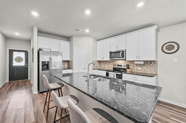 kitchen with sink, a kitchen island with sink, stainless steel appliances, a kitchen breakfast bar, and white cabinets