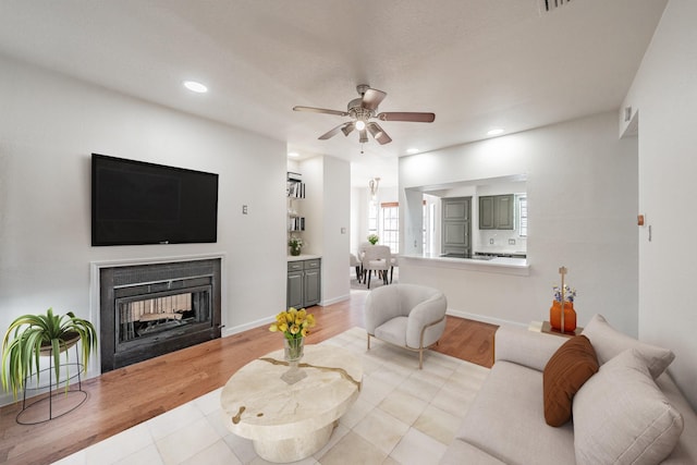 living room with light wood-type flooring, ceiling fan, and a multi sided fireplace