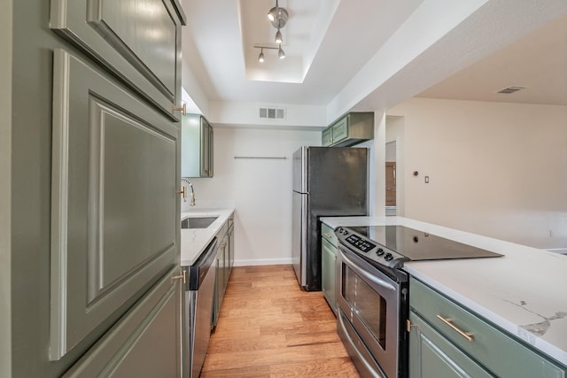 kitchen featuring appliances with stainless steel finishes, rail lighting, sink, green cabinets, and light hardwood / wood-style floors