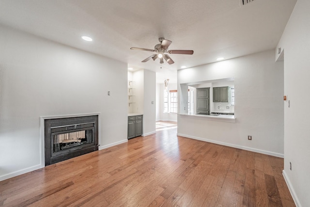 unfurnished living room with a multi sided fireplace, ceiling fan, and light hardwood / wood-style flooring