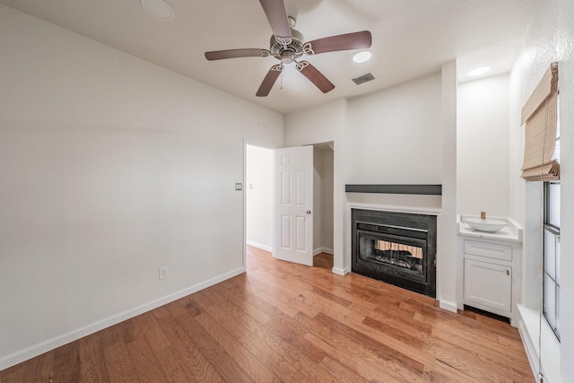 unfurnished living room featuring ceiling fan, a multi sided fireplace, and light hardwood / wood-style flooring