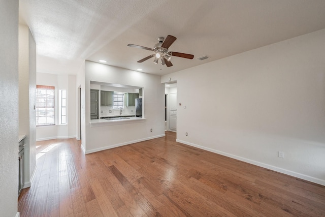 unfurnished living room featuring ceiling fan, a textured ceiling, and light hardwood / wood-style floors