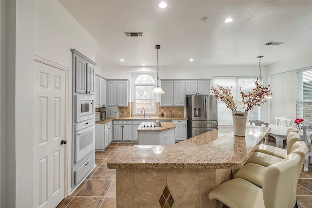 kitchen with sink, white appliances, gray cabinetry, light stone counters, and a kitchen island