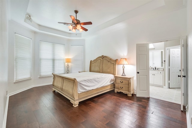 bedroom with a raised ceiling, ceiling fan, dark wood-type flooring, and ensuite bath