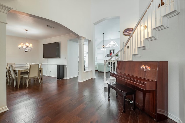 foyer entrance with crown molding, ceiling fan with notable chandelier, dark wood-type flooring, and ornate columns