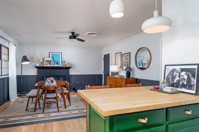 kitchen with wood counters, green cabinetry, decorative light fixtures, light hardwood / wood-style flooring, and a fireplace