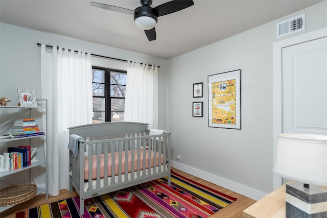 bedroom featuring hardwood / wood-style flooring, a crib, and ceiling fan