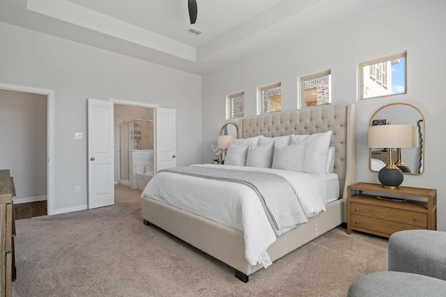 carpeted bedroom featuring ensuite bathroom, ceiling fan, visible vents, baseboards, and a tray ceiling