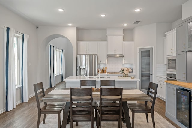 dining area with arched walkways, beverage cooler, visible vents, and light wood finished floors