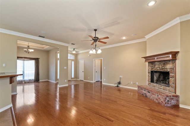 unfurnished living room featuring hardwood / wood-style flooring, ornamental molding, a stone fireplace, and ceiling fan with notable chandelier