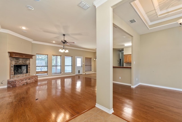 unfurnished living room with crown molding, a fireplace, ceiling fan with notable chandelier, and light hardwood / wood-style flooring