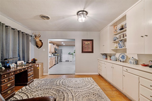 kitchen with stainless steel fridge, a textured ceiling, light hardwood / wood-style flooring, and white cabinets