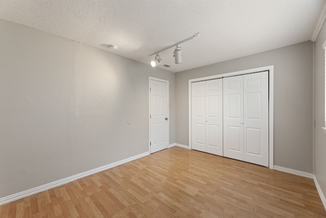 unfurnished bedroom with rail lighting, a closet, a textured ceiling, and light wood-type flooring