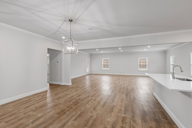 unfurnished living room with sink, a notable chandelier, wood-type flooring, and ornamental molding