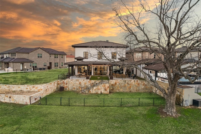 back house at dusk with a lawn and a patio