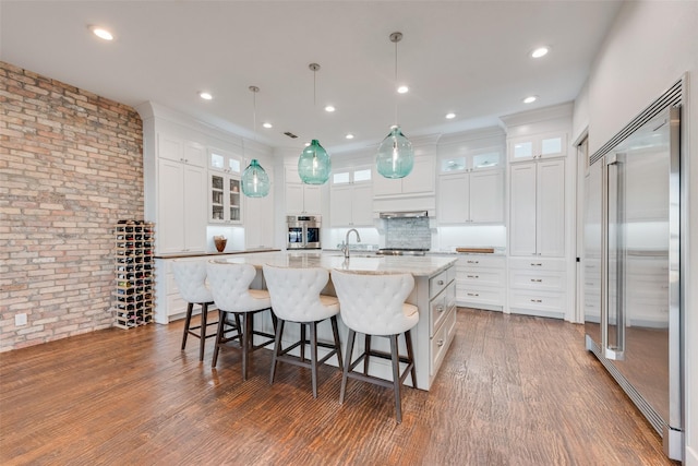 kitchen with light stone counters, a center island with sink, pendant lighting, stainless steel appliances, and white cabinets