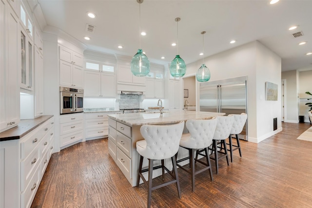 kitchen featuring a spacious island, white cabinetry, light stone counters, decorative light fixtures, and stainless steel appliances