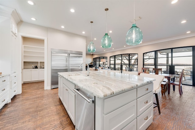 kitchen with sink, white cabinets, hanging light fixtures, stainless steel appliances, and a spacious island