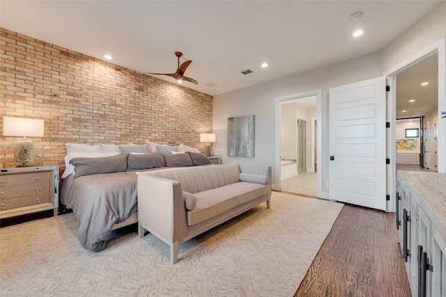 bedroom featuring ceiling fan, ensuite bath, brick wall, and light hardwood / wood-style flooring