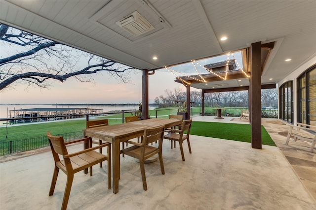 patio terrace at dusk featuring a lawn and a water view