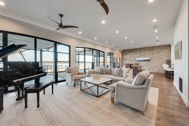 living room featuring crown molding, light hardwood / wood-style floors, ceiling fan, and brick wall