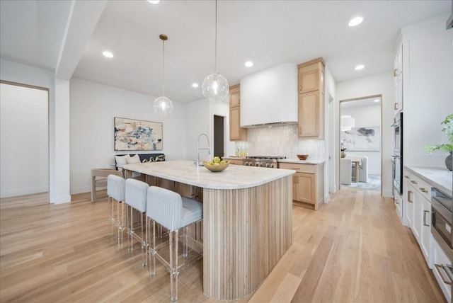 kitchen featuring hanging light fixtures, tasteful backsplash, custom range hood, a center island with sink, and light wood-type flooring