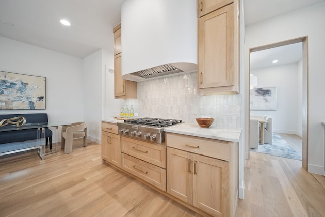 kitchen featuring light brown cabinetry, custom exhaust hood, stainless steel gas stovetop, light hardwood / wood-style floors, and decorative backsplash