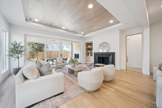 living room featuring hardwood / wood-style floors, built in features, and a raised ceiling