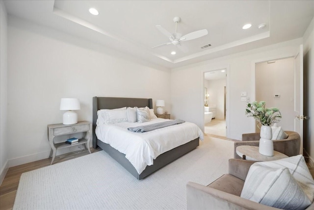 bedroom featuring a raised ceiling, wood-type flooring, ensuite bathroom, and ceiling fan