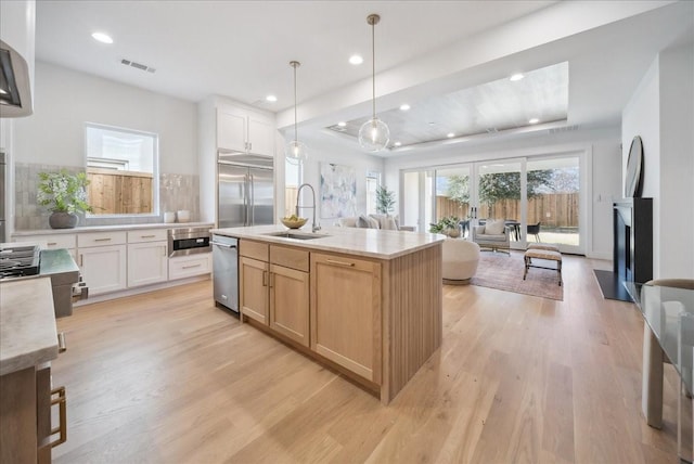 kitchen featuring sink, appliances with stainless steel finishes, a kitchen island with sink, white cabinetry, and decorative light fixtures