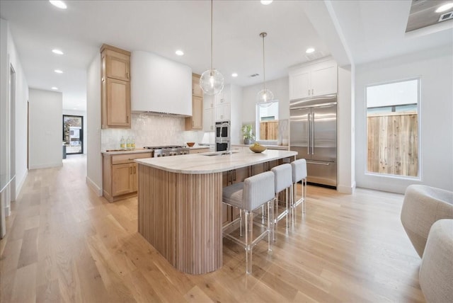 kitchen with a breakfast bar, sink, decorative backsplash, stainless steel appliances, and a center island with sink