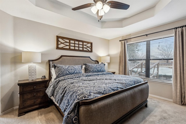 bedroom with light colored carpet, a raised ceiling, and ceiling fan