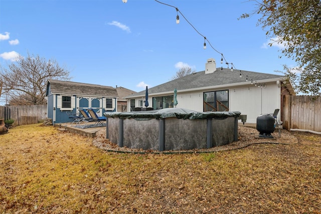 rear view of property with an outbuilding, a yard, and a covered pool