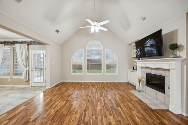 unfurnished living room featuring a tiled fireplace, light hardwood / wood-style flooring, ceiling fan, and vaulted ceiling