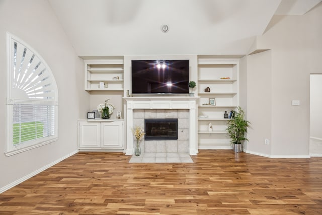 unfurnished living room featuring a tiled fireplace, built in features, and light wood-type flooring