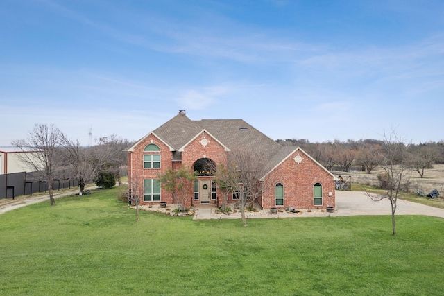 traditional-style house with roof with shingles, a front yard, and brick siding