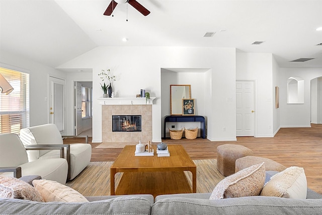 living room featuring ceiling fan, vaulted ceiling, a tile fireplace, and light wood-type flooring