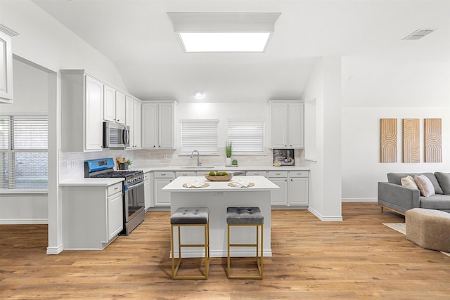 kitchen featuring sink, a breakfast bar, appliances with stainless steel finishes, a center island, and vaulted ceiling with skylight