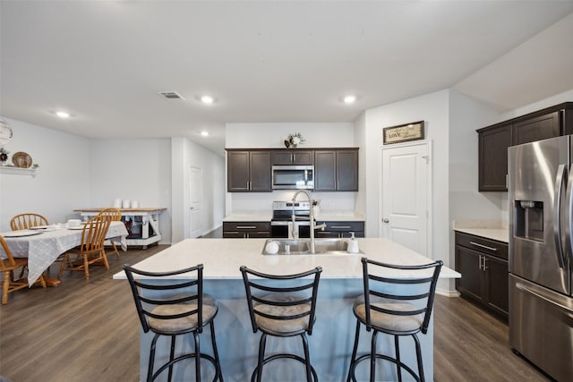 kitchen featuring sink, appliances with stainless steel finishes, dark brown cabinets, an island with sink, and dark hardwood / wood-style flooring