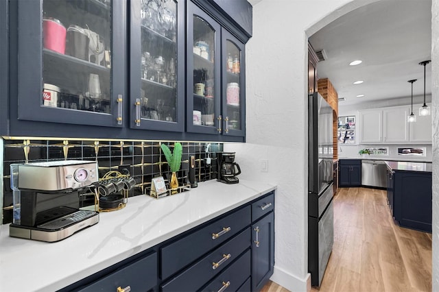 bar featuring pendant lighting, appliances with stainless steel finishes, backsplash, light stone counters, and light hardwood / wood-style floors