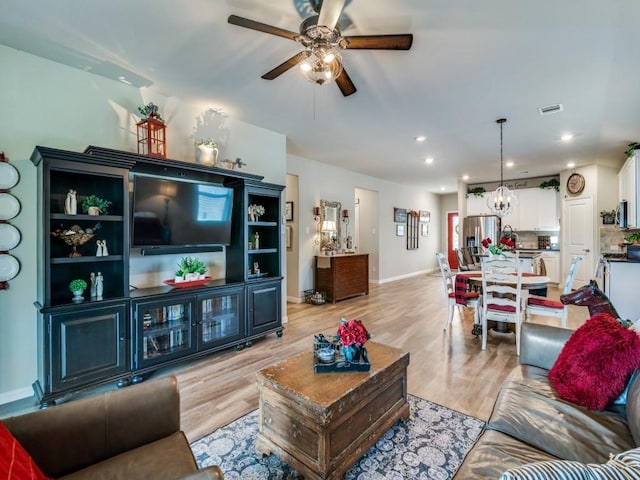 living room featuring ceiling fan with notable chandelier and light hardwood / wood-style floors