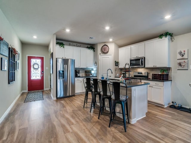 kitchen with a kitchen bar, white cabinetry, a center island with sink, light wood-type flooring, and stainless steel appliances