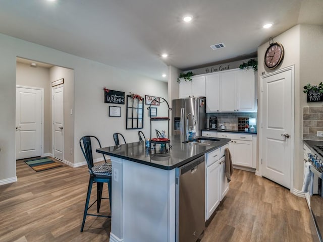 kitchen with sink, a breakfast bar area, appliances with stainless steel finishes, white cabinetry, and a center island with sink