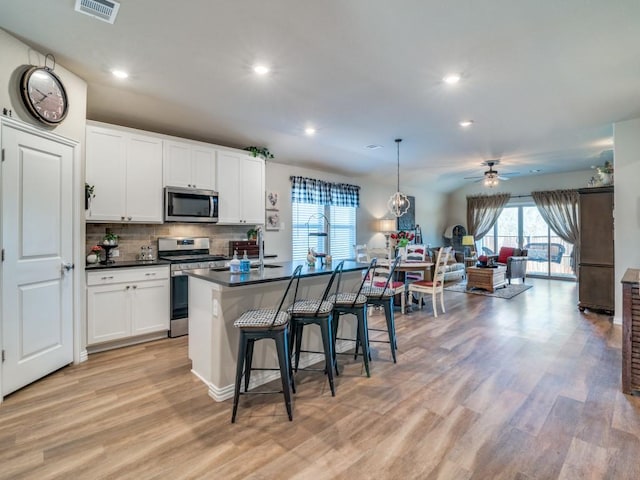 kitchen featuring a kitchen island with sink, hanging light fixtures, stainless steel appliances, and white cabinets